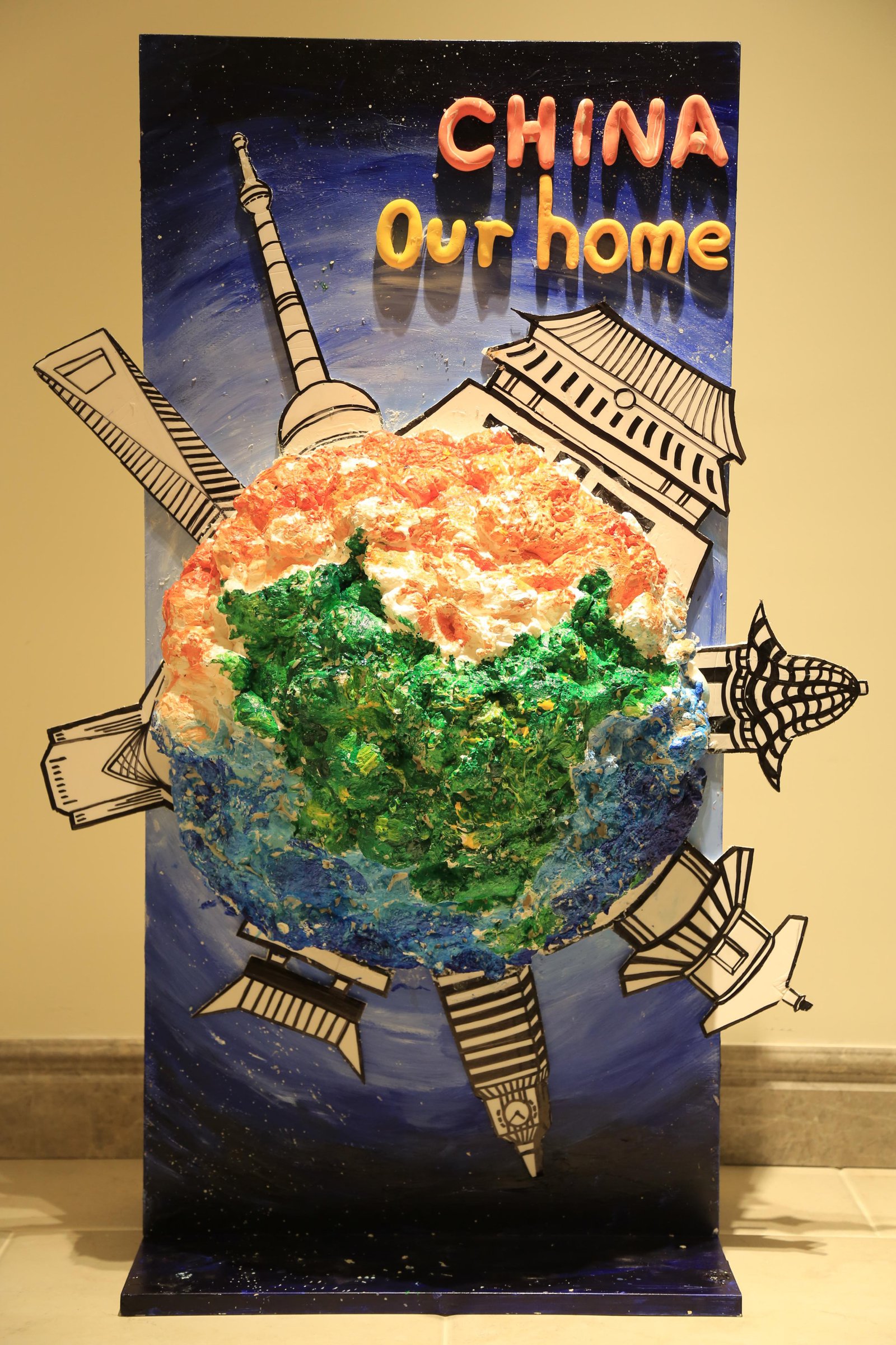 Mixed media relief sculpture of a globe ringed by paper landmarks, titled China Our Home