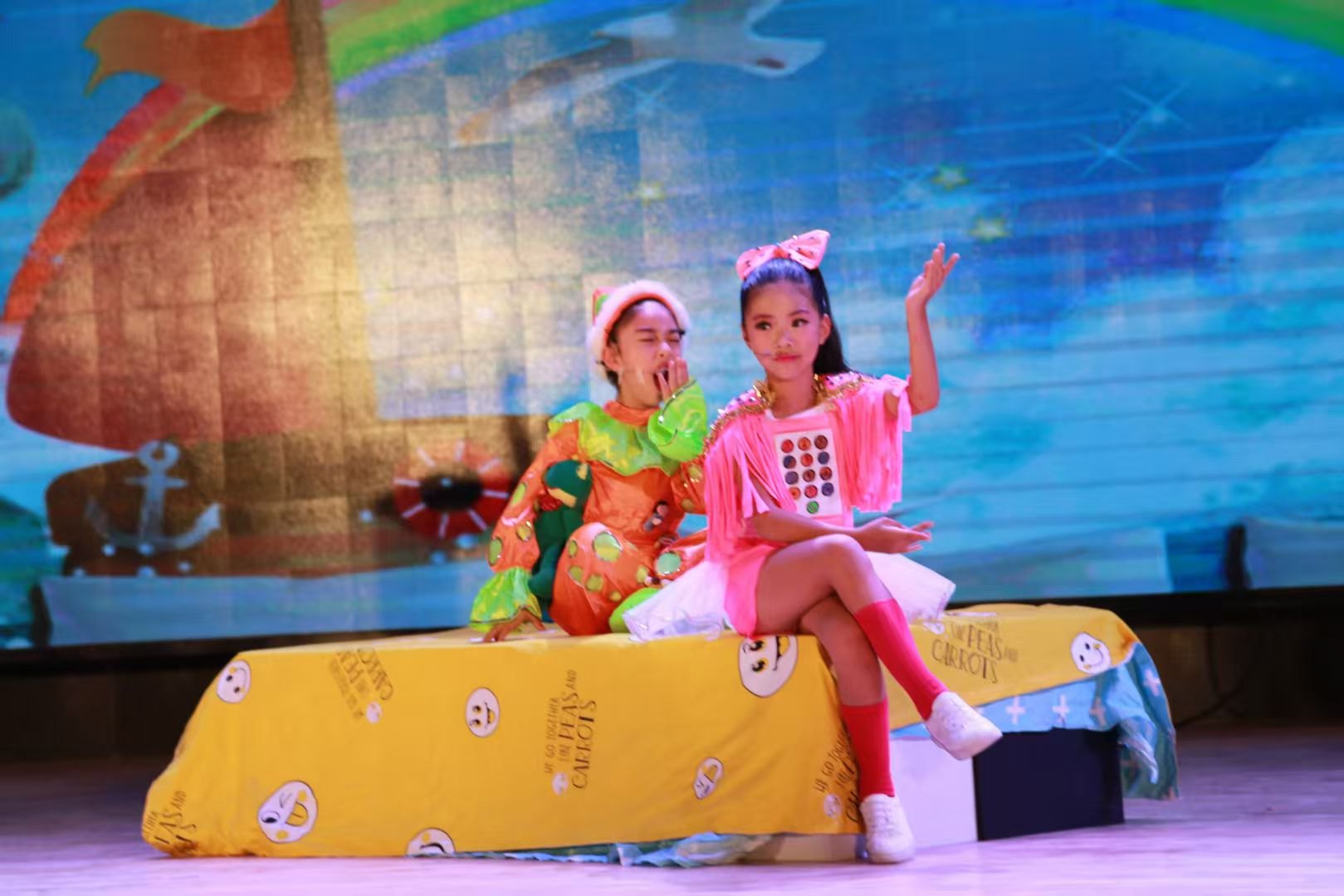 Two performers in bright costumes on a storybook stage set