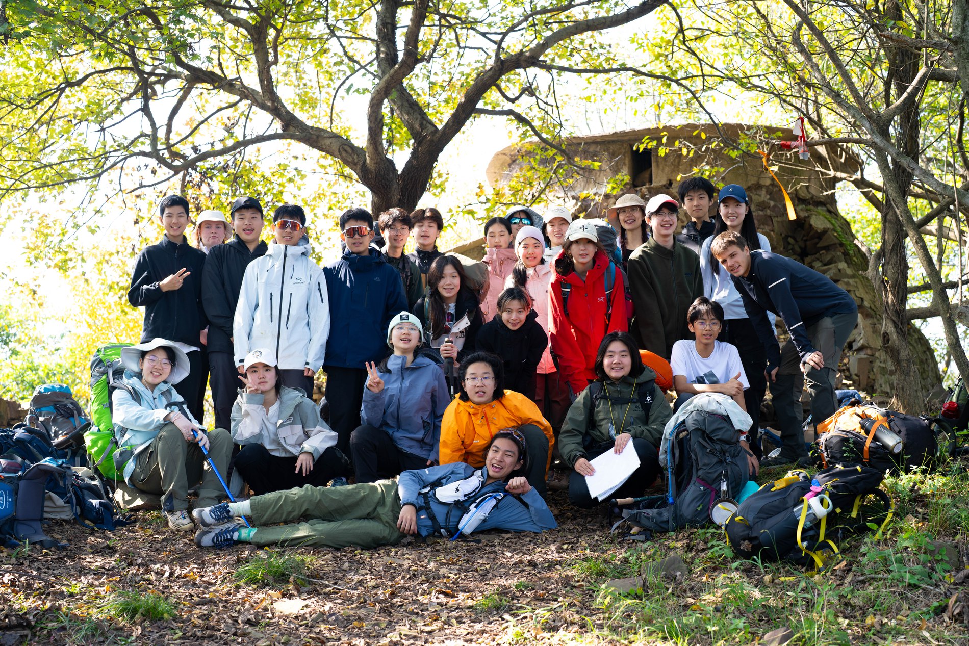 Large group hiking trip, posing near an old stone structure in the woods